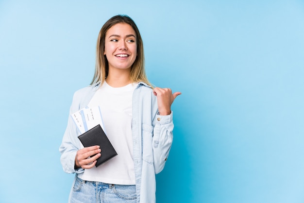 Joven mujer caucásica sosteniendo un pasaporte puntos aislados con el dedo pulgar, riendo y despreocupado.