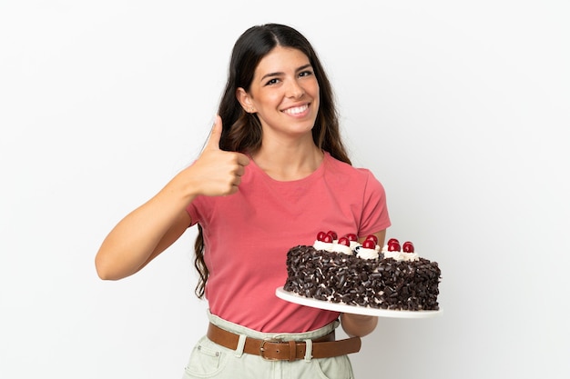 Joven mujer caucásica sosteniendo pastel de cumpleaños aislado sobre fondo blanco dando un pulgar hacia arriba gesto