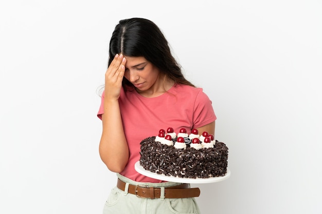 Joven mujer caucásica sosteniendo pastel de cumpleaños aislado sobre fondo blanco con dolor de cabeza