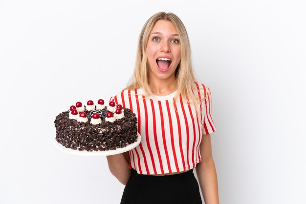 Joven mujer caucásica sosteniendo pastel de cumpleaños aislado sobre fondo blanco con expresión facial sorpresa