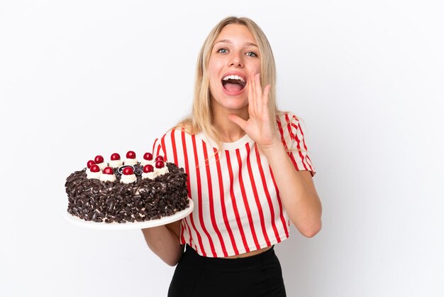 Joven mujer caucásica sosteniendo pastel de cumpleaños aislado sobre fondo blanco gritando con la boca abierta