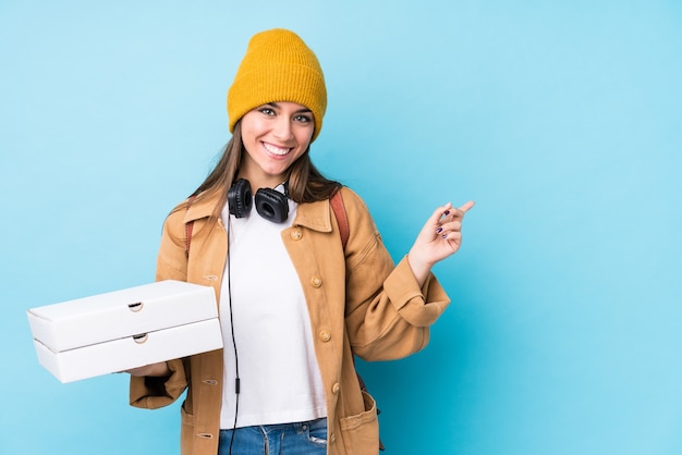 Joven mujer caucásica sosteniendo pizzas aisladas sonriendo y apuntando a un lado, mostrando algo en el espacio en blanco.