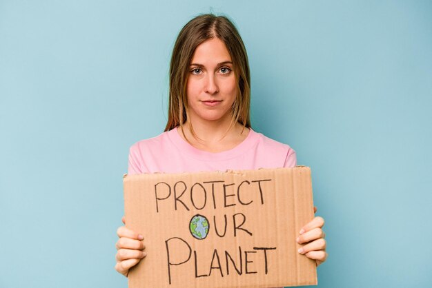 Joven mujer caucásica sosteniendo proteger su planeta cartel aislado sobre fondo azul.