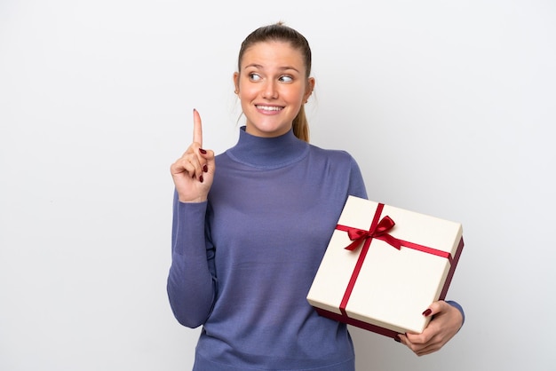 Joven mujer caucásica sosteniendo un regalo aislado de fondo blanco con la intención de darse cuenta de la solución mientras levanta un dedo