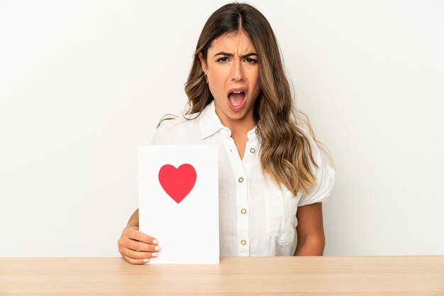 Joven mujer caucásica sosteniendo una tarjeta del día de San Valentín aislada gritando muy enojada y agresiva.