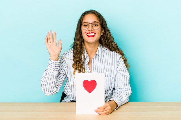 Foto joven mujer caucásica sosteniendo una tarjeta del día de san valentín aislada recibiendo una agradable sorpresa, emocionada y levantando las manos.