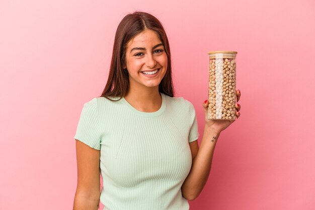 Joven mujer caucásica sosteniendo un tarro de garbanzos aislado sobre fondo rosa feliz, sonriente y alegre.