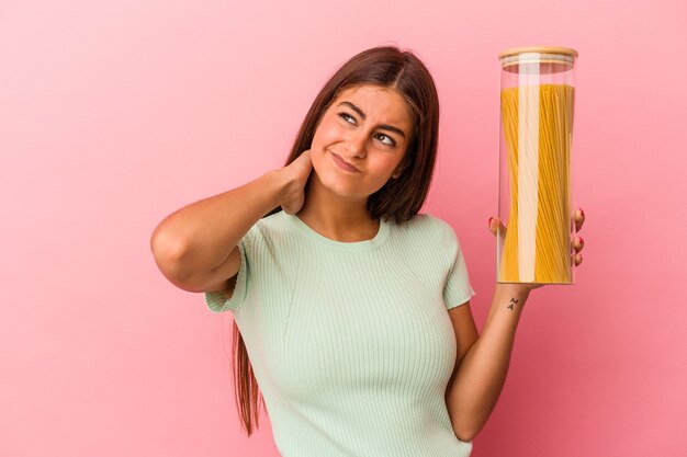 Joven mujer caucásica sosteniendo un tarro de pasta aislado en la pared rosa tocando la parte posterior de la cabeza, pensando y tomando una decisión.