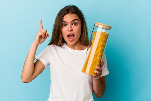 Joven mujer caucásica sosteniendo un tarro de pasta aislado sobre fondo azul con una idea, concepto de inspiración.