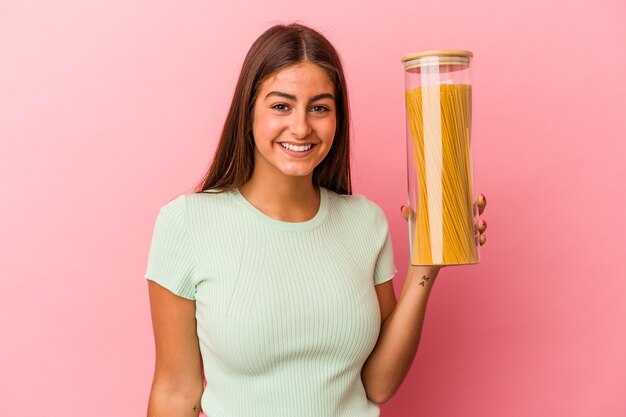 Joven mujer caucásica sosteniendo un tarro de pasta aislado sobre fondo rosa feliz, sonriente y alegre.