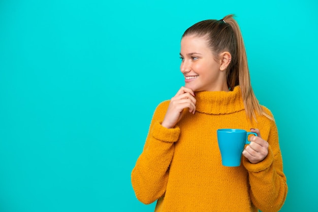 Joven mujer caucásica sosteniendo una taza aislada de fondo azul pensando en una idea y mirando de lado