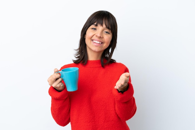 Joven mujer caucásica sosteniendo una taza de café aislada de fondo blanco estrechando la mano para cerrar un buen trato