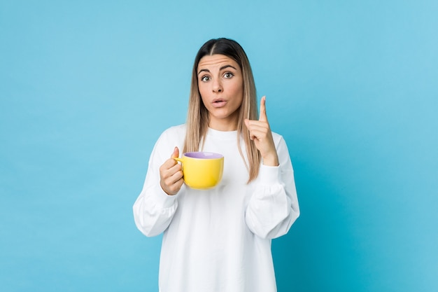 Joven mujer caucásica sosteniendo una taza de café con una gran idea, concepto de creatividad.