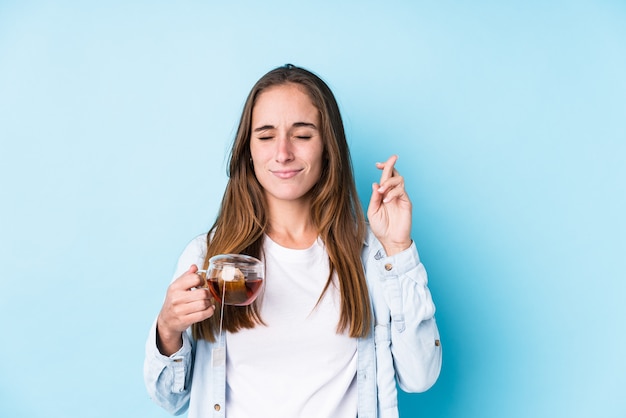 Joven mujer caucásica sosteniendo un té cruzando los dedos para tener suerte