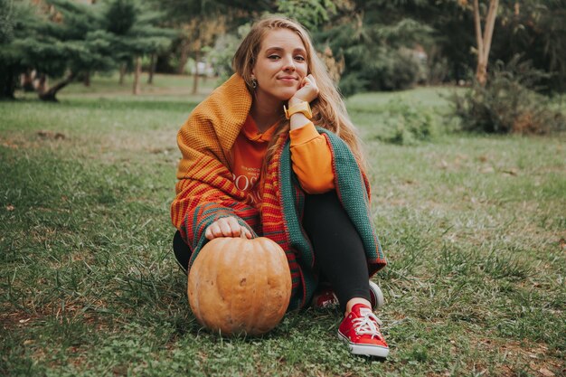 Joven mujer caucásica en sudadera con capucha naranja sosteniendo una calabaza naranja en sus manos en el jardín. Concepto de otoño