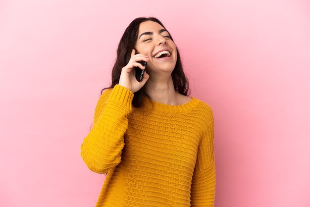 Joven mujer caucásica mediante teléfono móvil aislado en la pared rosa riendo