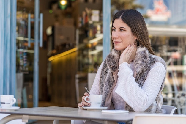 Joven mujer caucásica tomando café en una terraza con el móvil sobre la mesa