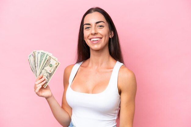 Joven mujer caucásica tomando mucho dinero aislada de fondo rosa sonriendo mucho