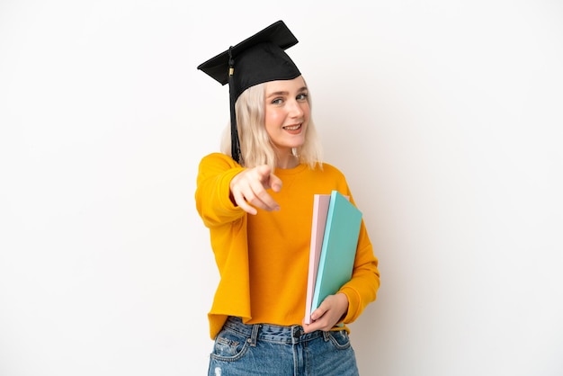 Joven mujer caucásica universitaria graduada aislada de fondo blanco apuntando al frente con expresión feliz