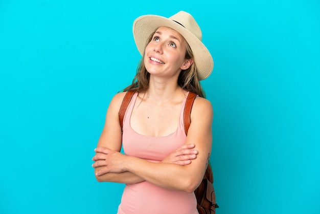 Joven mujer caucásica en vacaciones de verano aislada de fondo azul mirando hacia arriba mientras sonríe