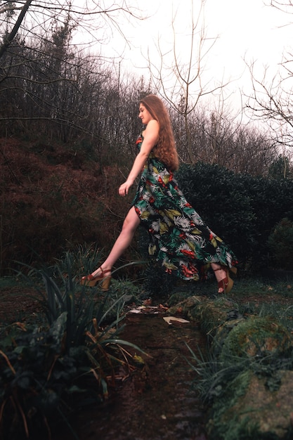 Joven mujer caucásica con un vestido colorido en medio del bosque junto a un pequeño río