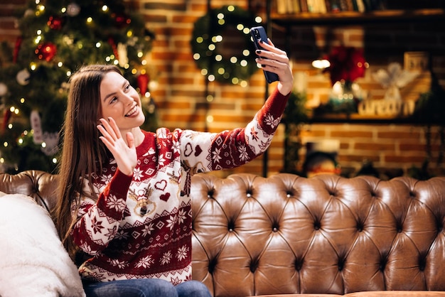 Joven mujer caucásica con videollamada de teléfono inteligente hablando con un amigo o novio árbol de navidad