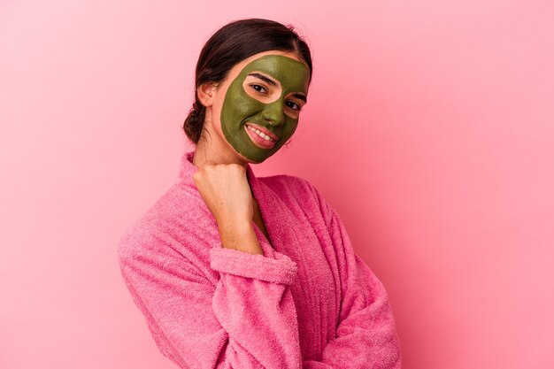 Joven mujer caucásica vistiendo una bata de baño y una máscara facial aislada sobre fondo rosa