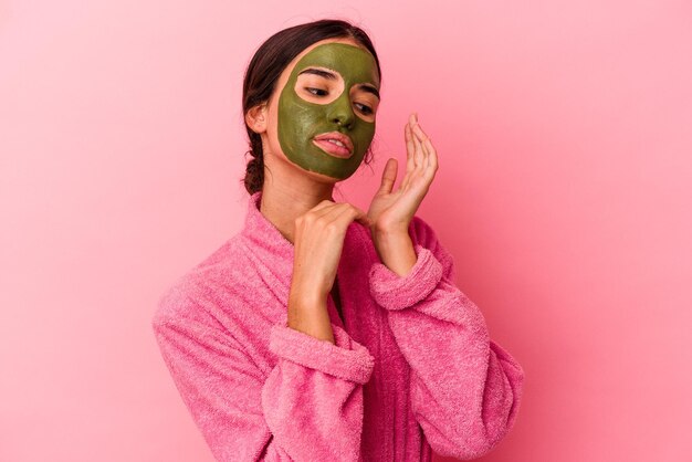 Foto joven mujer caucásica vistiendo una bata de baño y una máscara facial aislada sobre fondo rosa