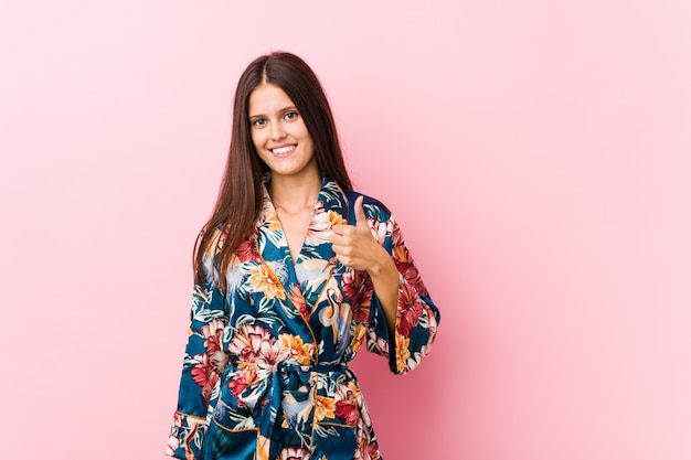 Joven mujer caucásica vistiendo un kimono pijama sonriendo y levantando el pulgar hacia arriba