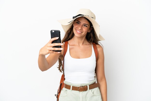 Foto joven mujer caucásica vistiendo una pamela en vacaciones de verano aislado sobre fondo blanco haciendo un selfie