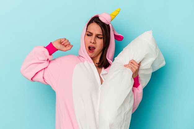 Joven mujer caucásica vistiendo un pijama de unicornio aislado sobre fondo azul.