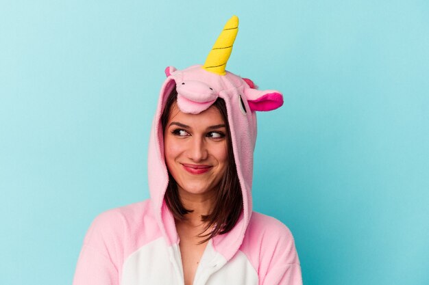 Joven mujer caucásica vistiendo un pijama de unicornio aislado sobre fondo azul.