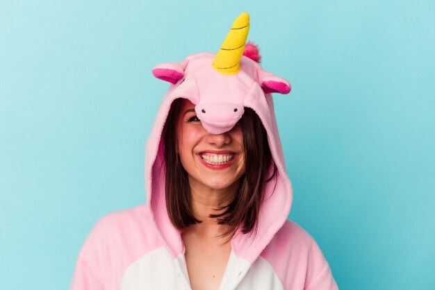 Joven mujer caucásica vistiendo un pijama de unicornio aislado sobre fondo azul.