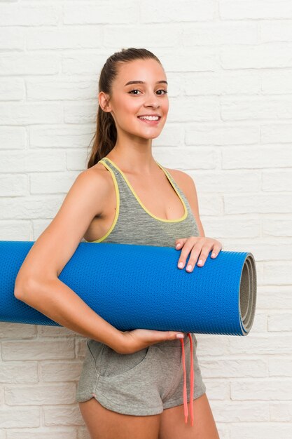 Joven mujer caucásica vistiendo ropa deportiva con una estera