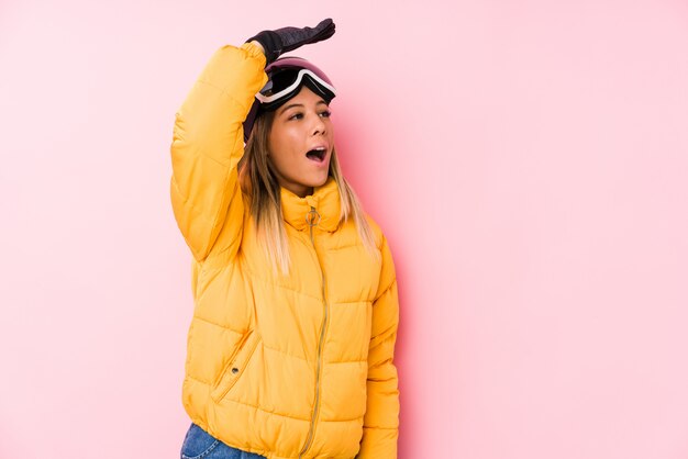 Joven mujer caucásica vistiendo ropa de esquí en una pared rosa mirando lejos manteniendo la mano en la frente.