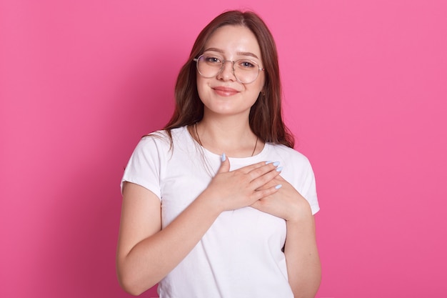 Joven mujer caucásica vistiendo t casual shirrt blanco, se encuentra sonriente con las manos en el pecho y agradecido gesto en la cara, con agradable expresión facial, aislado en la pared de color rosa. Concepto de salud