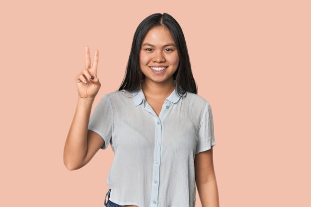 Joven mujer china aislada alegre y despreocupada mostrando un símbolo de paz con los dedos