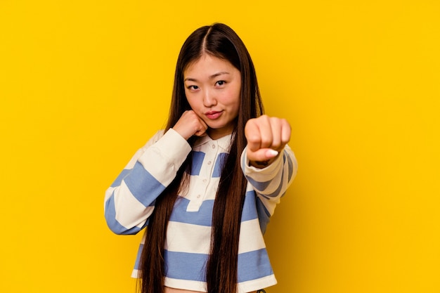 Joven mujer china aislada sobre fondo amarillo lanzando un puñetazo, ira, luchando debido a una discusión, boxeo.