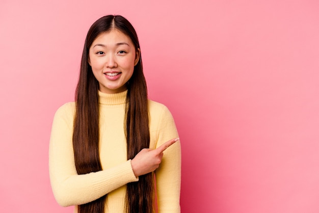 Joven mujer china aislada sobre fondo rosa sonriendo y apuntando a un lado, mostrando algo en el espacio en blanco.