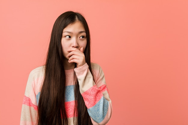 Joven mujer china fresca reflexiva cubriendo la boca con la mano