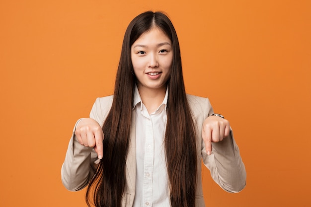 Joven mujer china de negocios apunta hacia abajo con los dedos, sentimiento positivo.