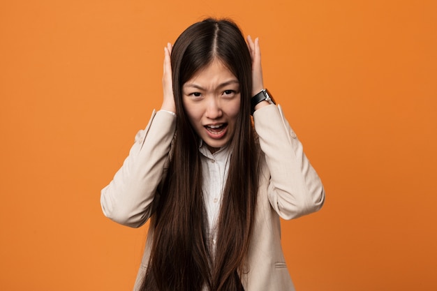 Joven mujer china de negocios que cubre los oídos con las manos tratando de no escuchar un sonido demasiado fuerte.