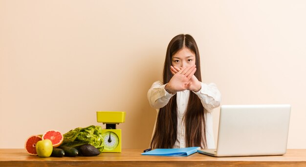 Joven mujer china nutricionista que trabaja con su computadora portátil haciendo un gesto de negación