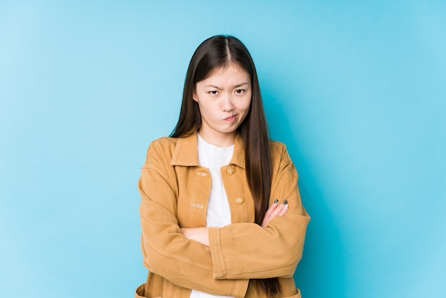 Joven mujer china posando en azul aislado con el ceño fruncido en disgusto, mantiene los brazos cruzados.