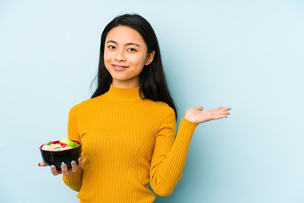 Joven mujer china sosteniendo fideos aislados relajado pensando en algo mirando un espacio de copia.