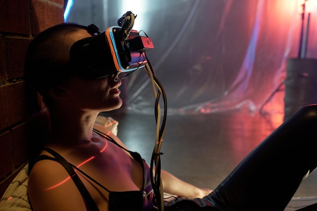 Joven mujer ciberpunk con gafas de realidad virtual jugando en línea en una habitación oscura