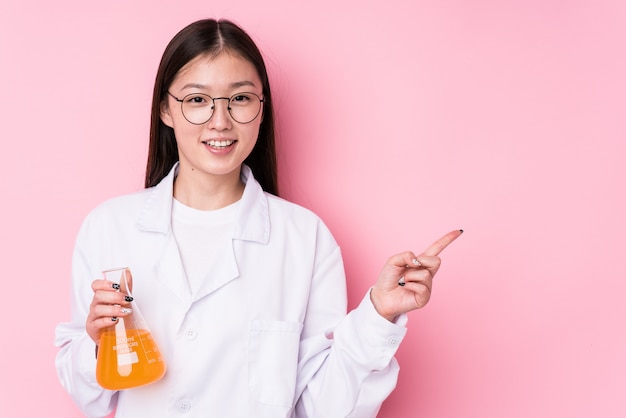 Joven mujer científica china aislada sonriendo y señalando a un lado, mostrando algo