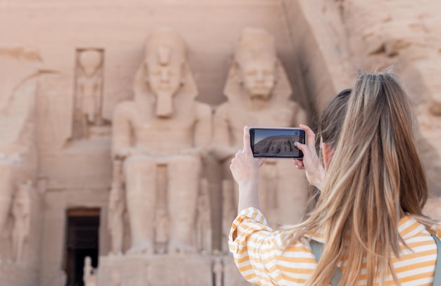 Joven mujer de cola de caballo irreconocible tomando una foto del hermoso monumento y el antiguo templo de Abu Simbel en Egipto