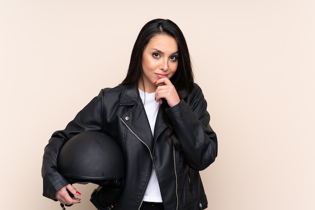 Joven mujer colombiana sosteniendo un casco de motocicleta sobre pared aislada riendo