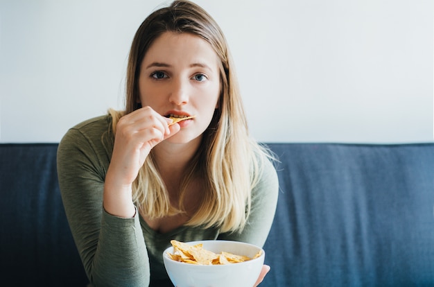 Joven mujer comiendo bocadillos en el sofá